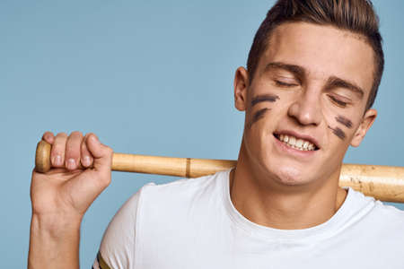 baseball guy with a bat in his hand on a blue background and a combat color on his face makeup model...