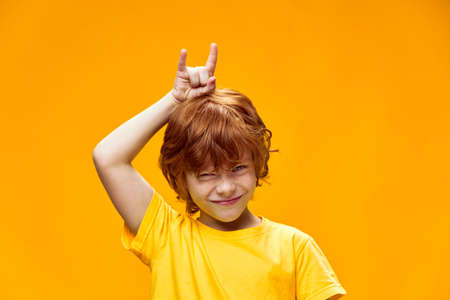 Expressive red-haired boy holding two fingers above the head of the hornsの写真素材