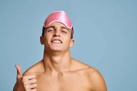 Relaxed man with pink sleep mask on blue background nude torso cropped view