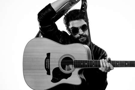 A man plays the guitar in a black leather jacket with sunglasses on a light backgroundの写真素材