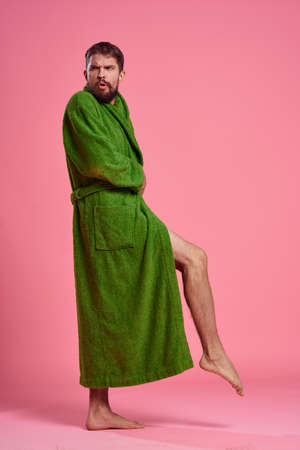 An emotional man in a green robe in full growth on a pink background gestures with his hands to the modelの写真素材
