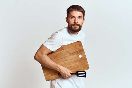 Man with a kitchen wooden board and with a shovel on a light background emotions white t-shirt model
