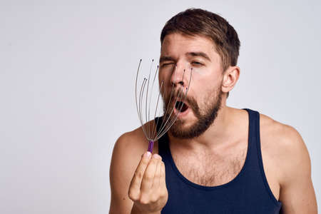 man with a massager for the head and in a blue t-shirt on a light background relaxing beard emotionsの写真素材