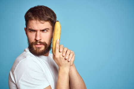 a man with a banana is caught in a white t-shirt on a blue background concept of communication by phoneの写真素材