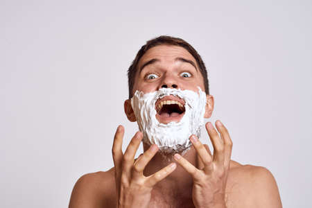 Handsome man with white shaving foam on his face and clean skin with razor grooming bare shoulders