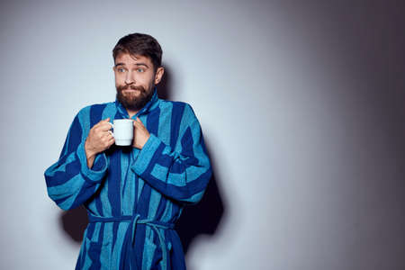 man in a blue robe with a white cup in his hand on a light background gesturing with his hands cropped viewの写真素材