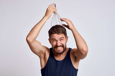 man with a massager for the head and in a blue t-shirt on a light background relaxing beard emotionsの写真素材
