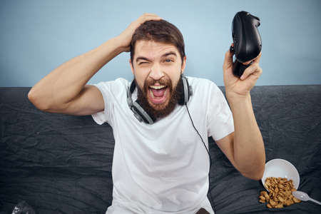 A man sits on a sofa with a gamepad in his hand. Leisure lifestyle game console