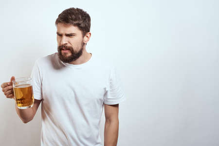 man with a mug of beer in his hands and a white t-shirt light background mustache beard emotions modelの写真素材