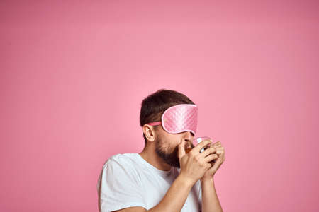 A man in a pink sleep mask with a cup of tea in his hands on an isolated background cropped viewの写真素材