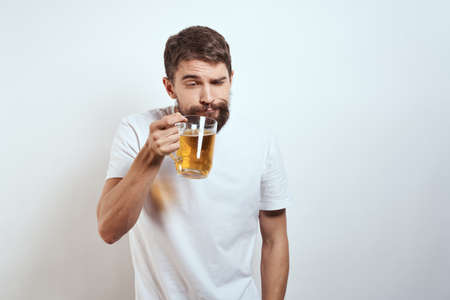man with a mug of beer in his hands and a white t-shirt light background mustache beard emotions modelの写真素材