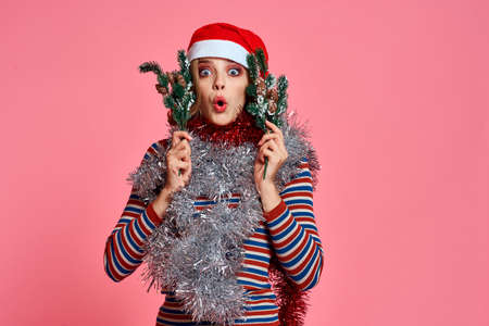 woman with christmas tree branches in hands red tinsel and festive hat pink background cropped view