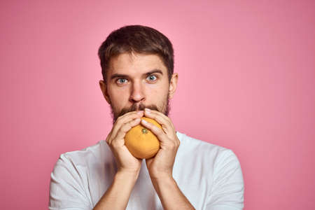 Young man with orange on a pink background in a white t-shirt emotions fun gesticulating with model handsの写真素材