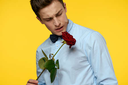 Gentleman in shirt and bow tie around his neck yellow background red roseの写真素材
