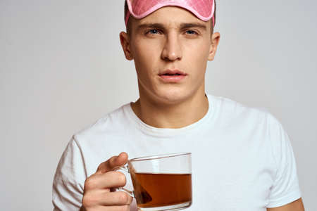 handsome man with pink sleep mask and with a cup of tea in hand pulls himself up on a light...