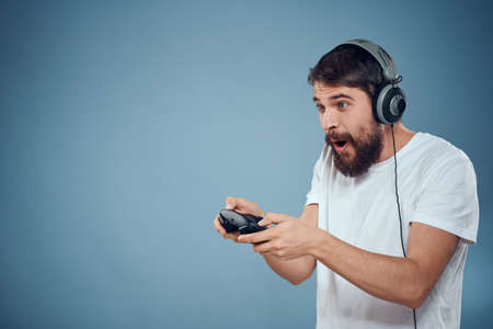 Man in headphones controller in hands playing game console lifestyle emotions blue background white t-shirtの写真素材
