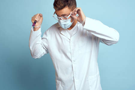 Doctor holds a syringe in his hand with a red liquid on a blue background medical gown and a protective maskの写真素材