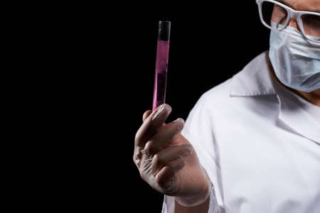 laboratory assistant in a medical mask and in a white coat with a liquid in a flask and a chemical on a black backgroundの写真素材