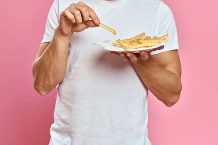 Man with French fries in a paper box on a pink background calories fast food portrait pink...