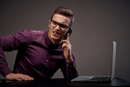 Male manager is sitting at the table and talking on the phone open laptop working office room