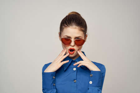 Fashionable woman in sunglasses and a blue shirt gesturing with her hands on a light background cropped viewの写真素材