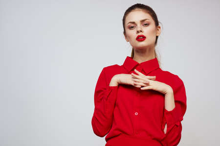A beautiful girl with red lips and a shirt on a light background gestures with her handsの写真素材