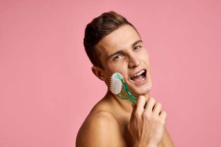 Handsome man with massager in hand on isolated pink background cropped view clean skinの写真素材