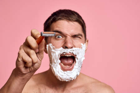 man with razor and white foam on his face pink background nude torso bathing treatments