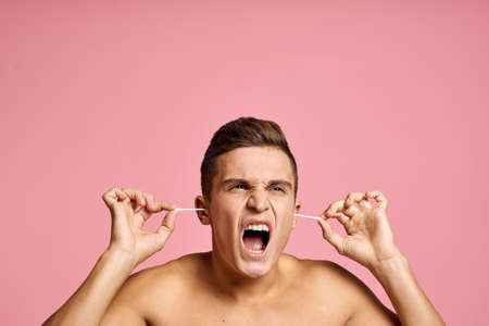 Emotional man with ear sticks in hands on pink background emotions cropped view of naked torsoの写真素材