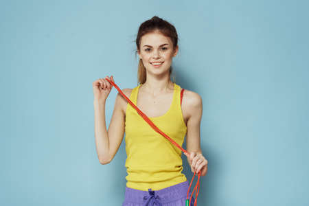 Sportive woman holding a skipping rope yellow tank top exercise gymnastics blue background