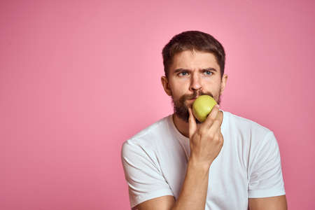 Cute man with an apple on a pink background gestures with his hands cropped white T-shirt Copy Spaceの写真素材