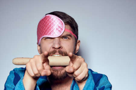 a man in a pink sleep mask holds a rolling pin in his hands and emotions energy aggression model blue robeの写真素材