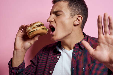 hungry man with hamburgers in hands fast food diet food emotions pink backgroundの写真素材