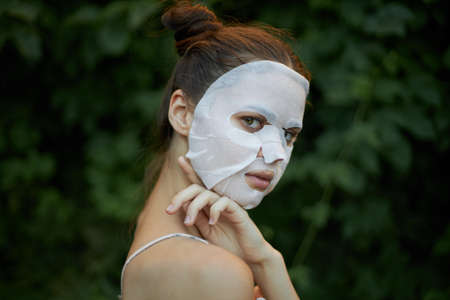 Portrait of a woman touches his shoulder with his hand white mask skin care bushes in the backgroundの写真素材