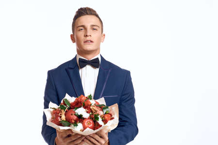 An elegant man in a classic suit with a bow tie holds a bouquet of flowers in his handの写真素材