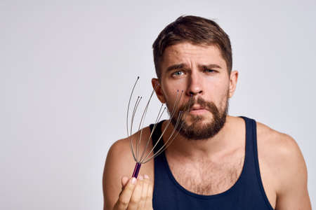 man with a massager for the head and in a blue t-shirt on a light background relaxing beard emotionsの写真素材