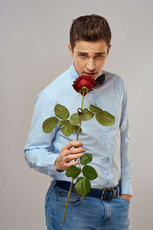 Romantic man with a red rose and in a blue shirt with a bow tie around his neck gray backgroundの写真素材