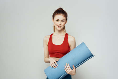 Woman holds in hand a mat for fitness sport slim figure exercises light backgroundの写真素材