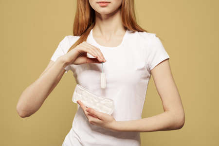 Girl with a tampon and a pad in her hand on a beige background cropped view of menstruation critical...
