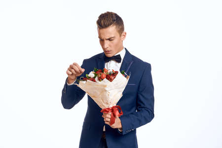 An elegant man in a classic suit with a bow tie holds a bouquet of flowers in his handの写真素材