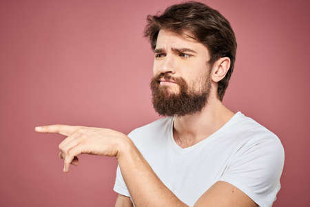 Emotional bearded man in white T-shirt discontent pink background