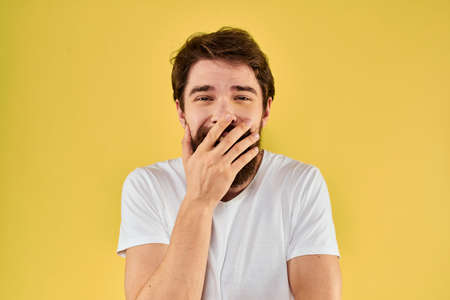 A man in a white t-shirt gestures with his hands lifestyle cropped view yellow background more fun