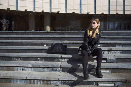 A woman in a leather jacket sits on the stairs near the theater on the street model