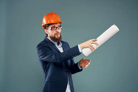 A man in a suit in an orange hard hat blueprints in the hands of a construction engineer