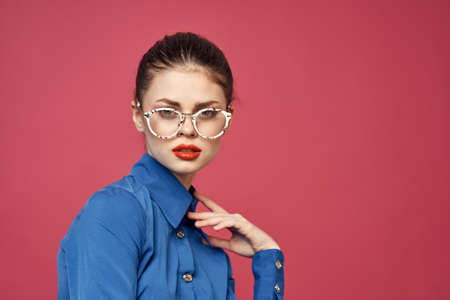 Portrait of a woman in glasses and in a blue shirt red lips pink background model