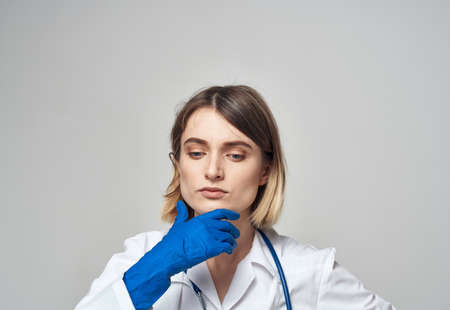 Emotional woman in blue medical gloves touches her head with her hands on a light backgroundの写真素材