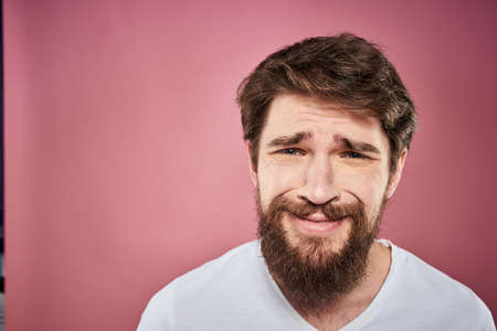 bearded man in white t-shirt emotions displeased facial expression studio pink backgroundの写真素材