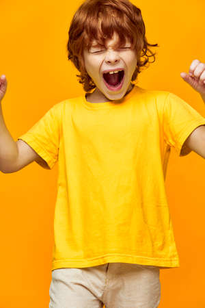 Energetic child with red hair screams against a yellow backgroundの写真素材