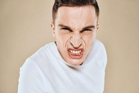 Man with displeased facial expression emotions white t-shirt gestures with hands beige backgroundの写真素材