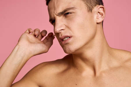 Emotional man with ear sticks in hands on pink background emotions cropped view of naked torsoの写真素材